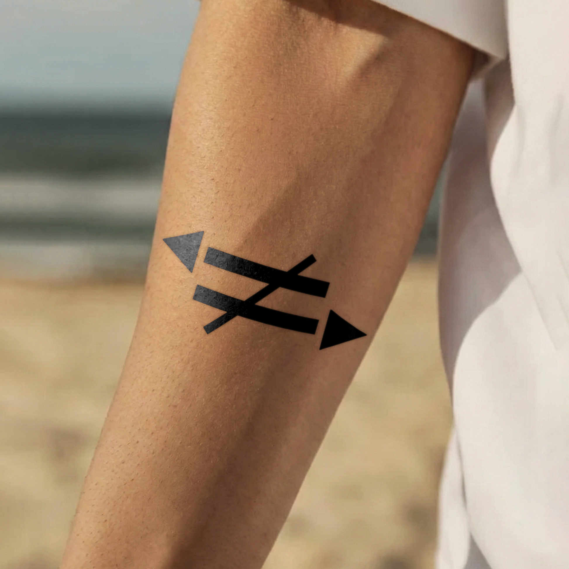 Black temporary tattoo of crossed arrows on a person's arm with a blurred natural background