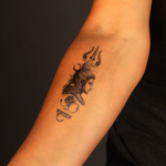 Tattoo of a deity's face with a trident on a person's arm against a black background