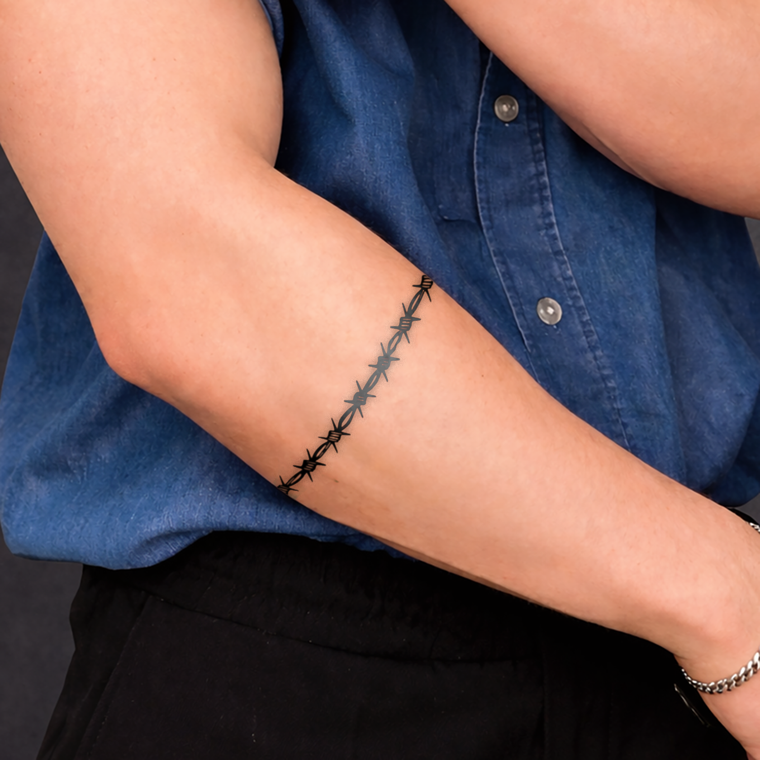 Person wearing a blue shirt with a barbed wire tattoo on their arm against a dark background