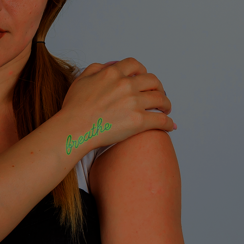 Person with a green 'breathe' tattoo on their wrist against a gray background