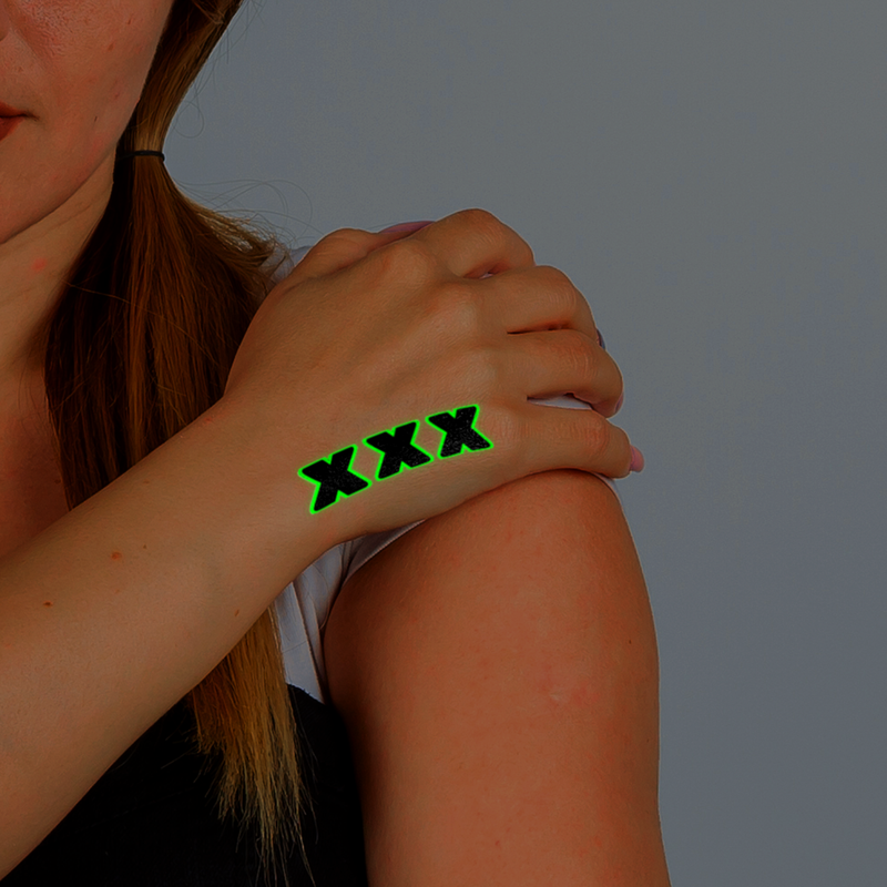 Person wearing a green 'XXX' temporary tattoo on their arm against a gray background