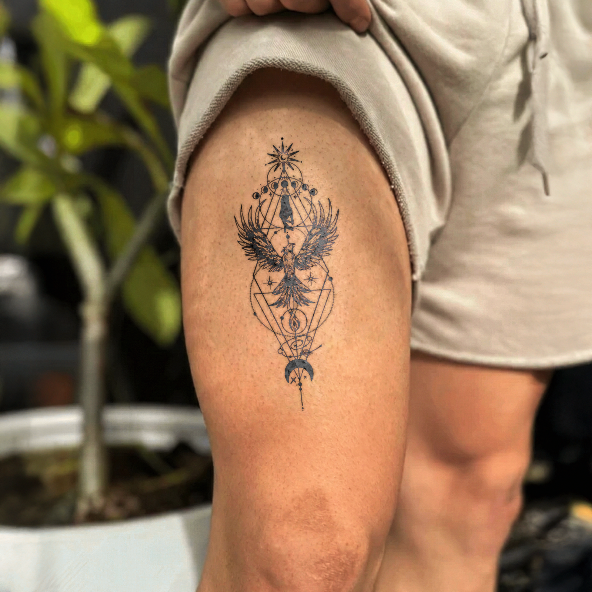 Tattoo of an eagle and geometric design on a person's leg with a blurred natural background