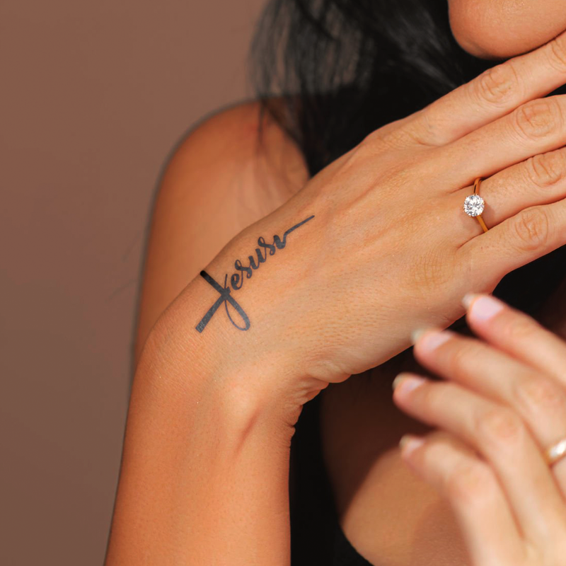 Hand with 'forever' tattoo on wrist against a neutral background