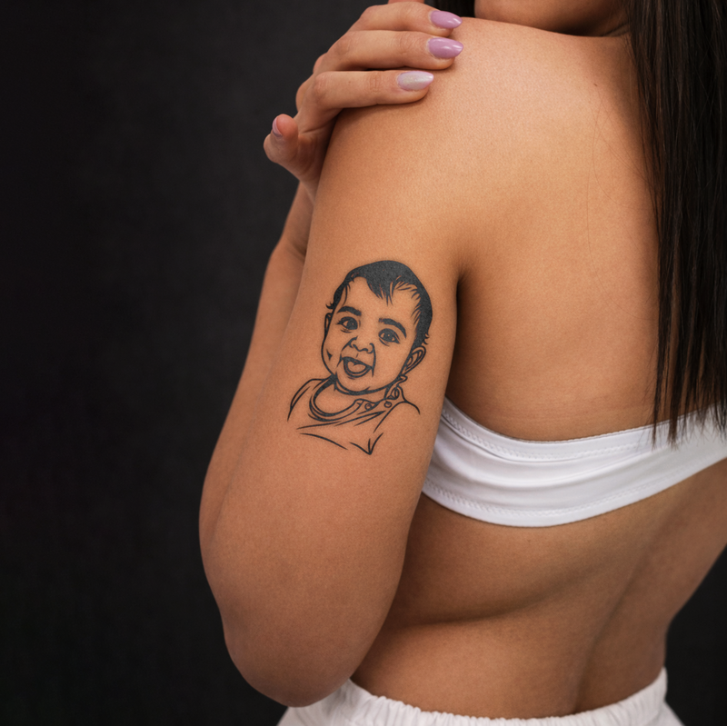 Person with a tattoo of a child on their arm against a dark background