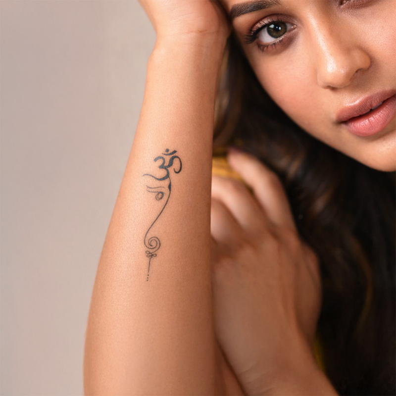 Woman with a tattoo of an Om symbol on her arm against a neutral background
