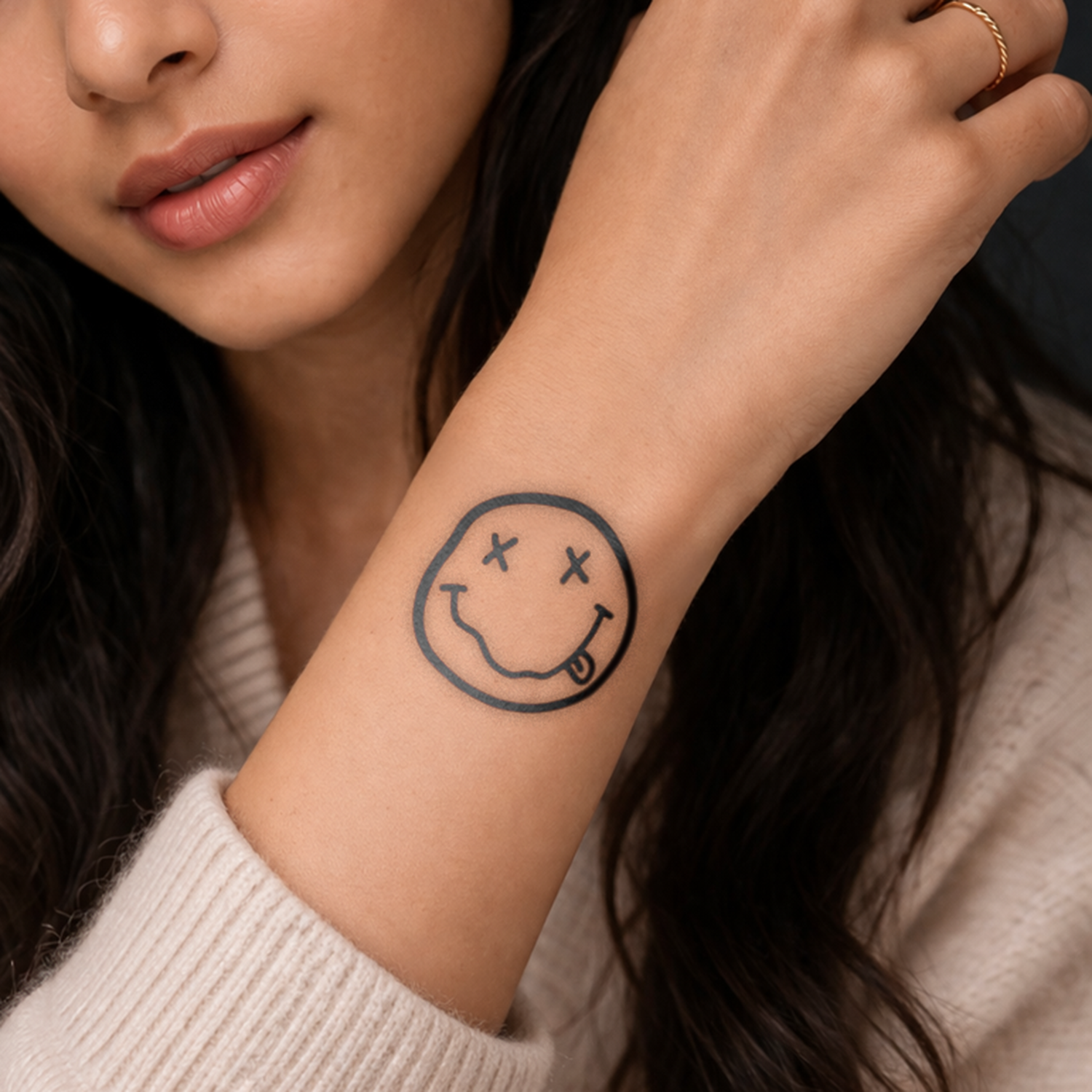 Close-up of a person's arm with a smiley face tattoo, wearing a beige sweater.