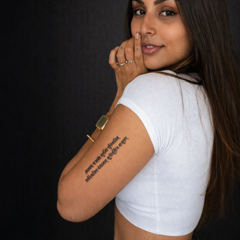 Woman wearing a white t-shirt with a visible tattoo on her arm against a dark background