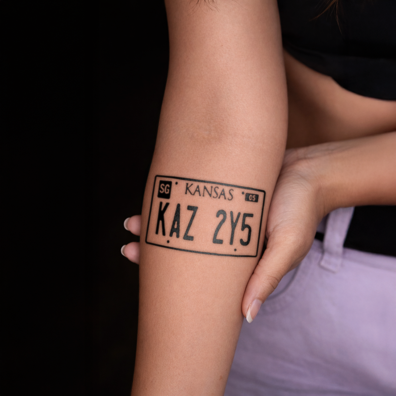 Tattoo of a Kansas license plate design on a person's arm against a dark background