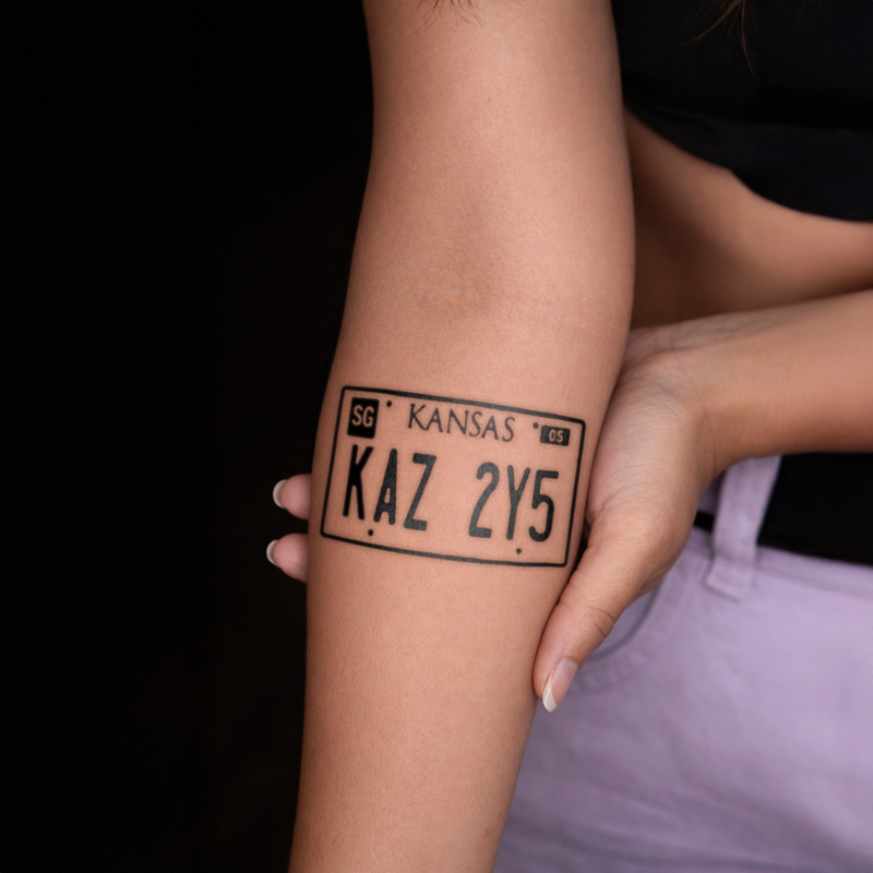 Tattoo of a Kansas license plate design on a person's arm against a dark background
