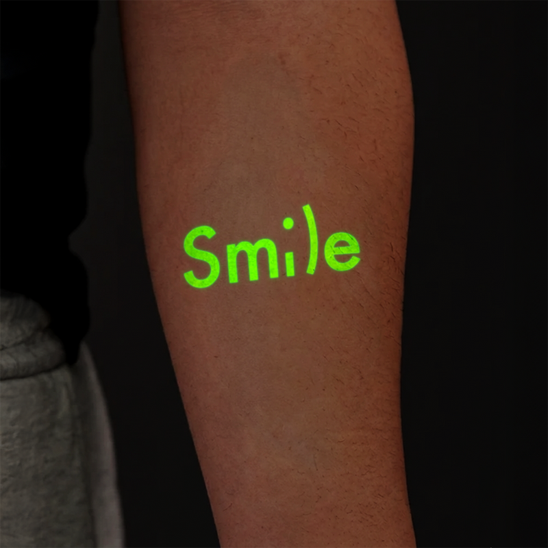 Green 'Smile' tattoo on a person's arm with a dark background