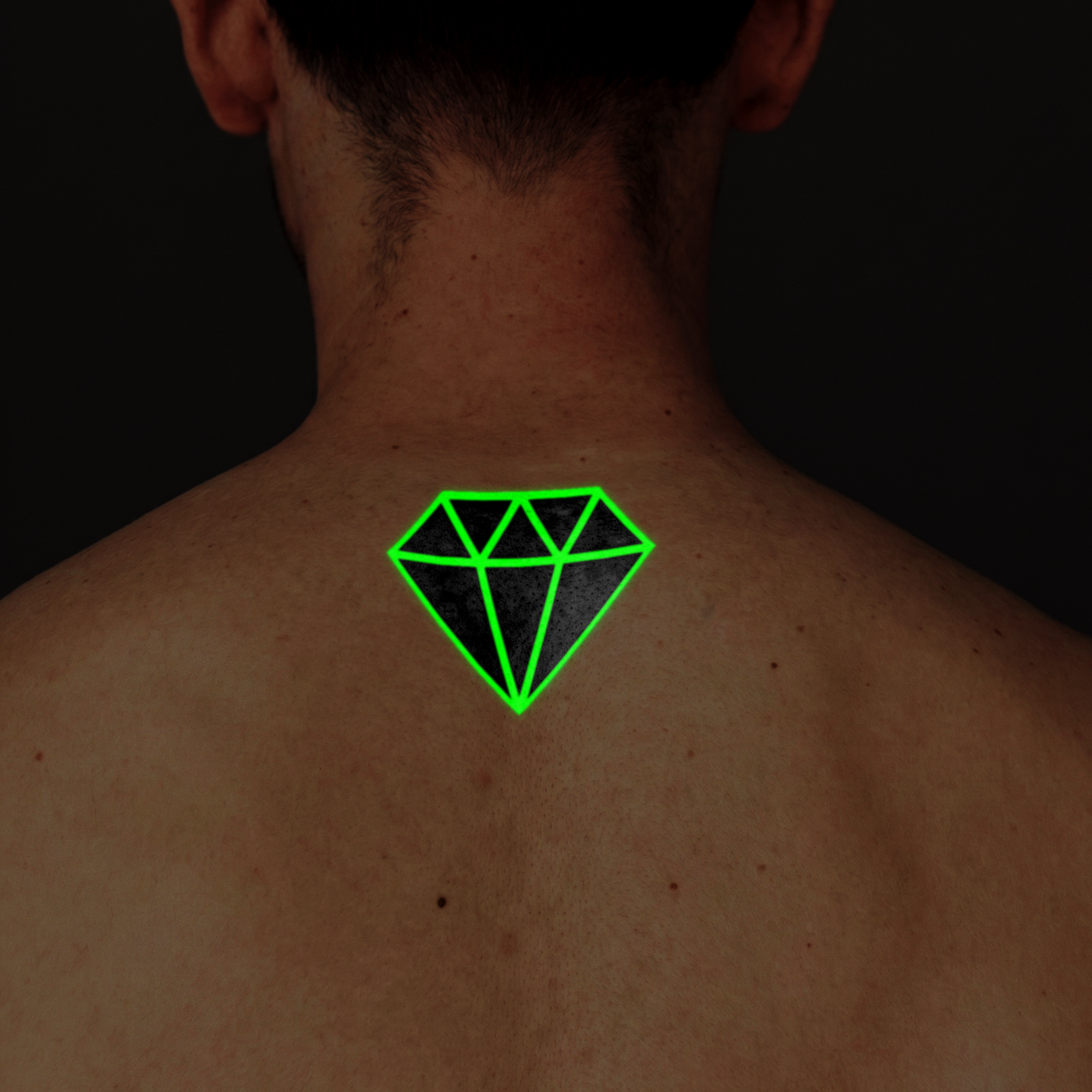 Green diamond-shaped tattoo on a person's back against a dark background