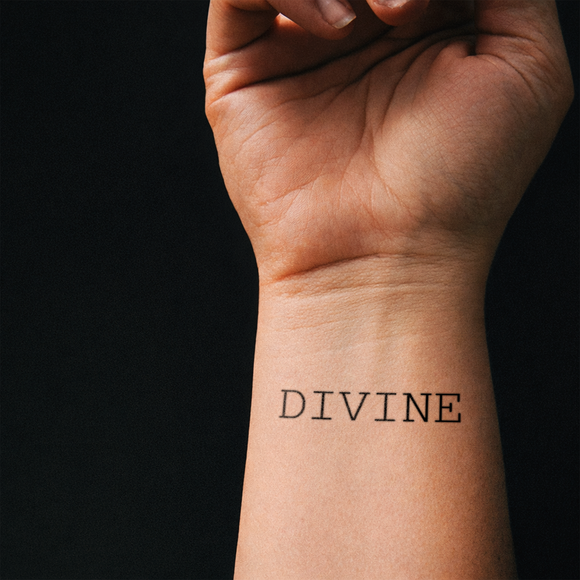 Hand with 'DIVINE' tattoo on wrist against a black background