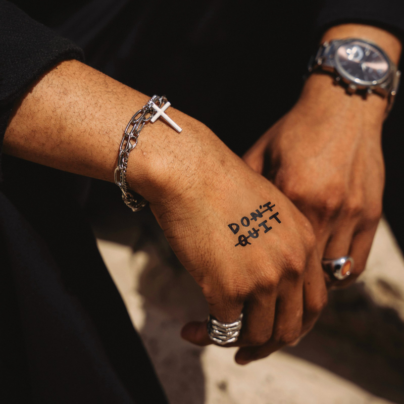 Close-up of a person's hands with tattoos and jewelry on a dark background