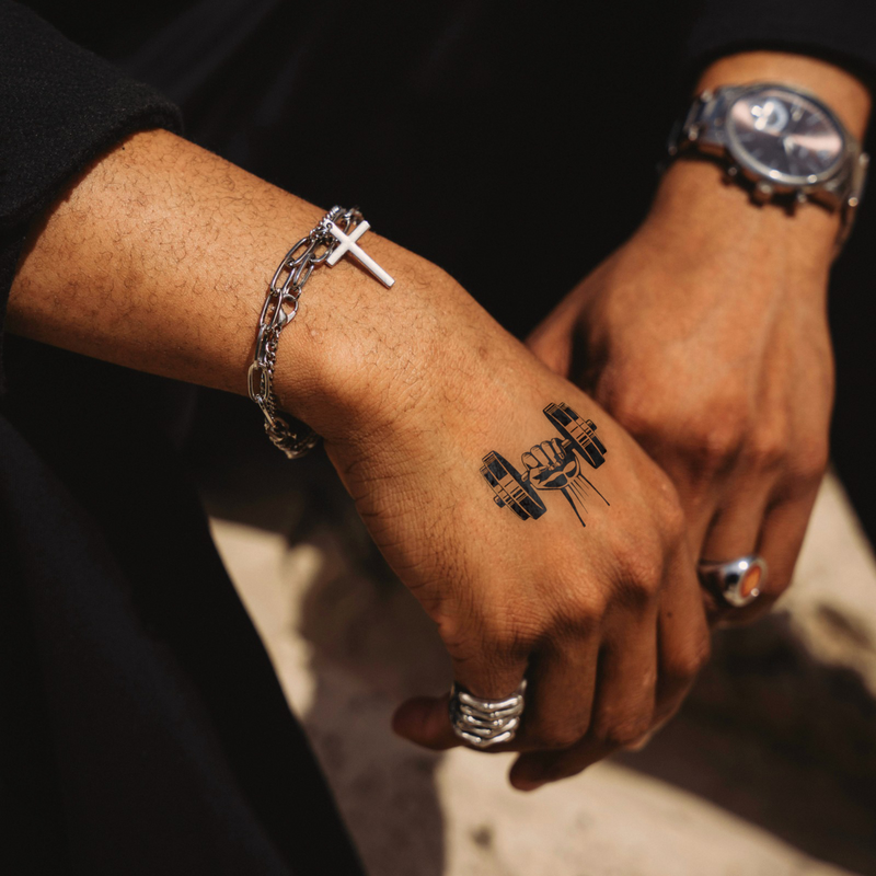 Close-up of a person's hands with tattoos, bracelets, and a watch on a dark background