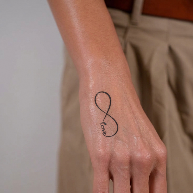 Hand with an infinity symbol tattoo on a plain background