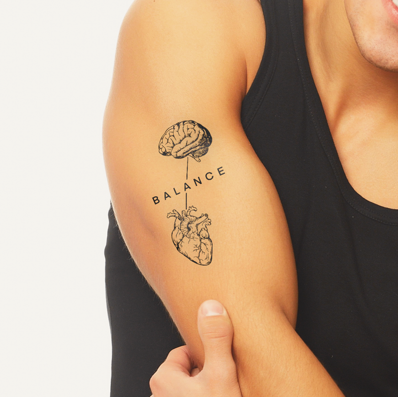 Tattoo of a brain and heart with 'BALANCE' text on a person's arm.