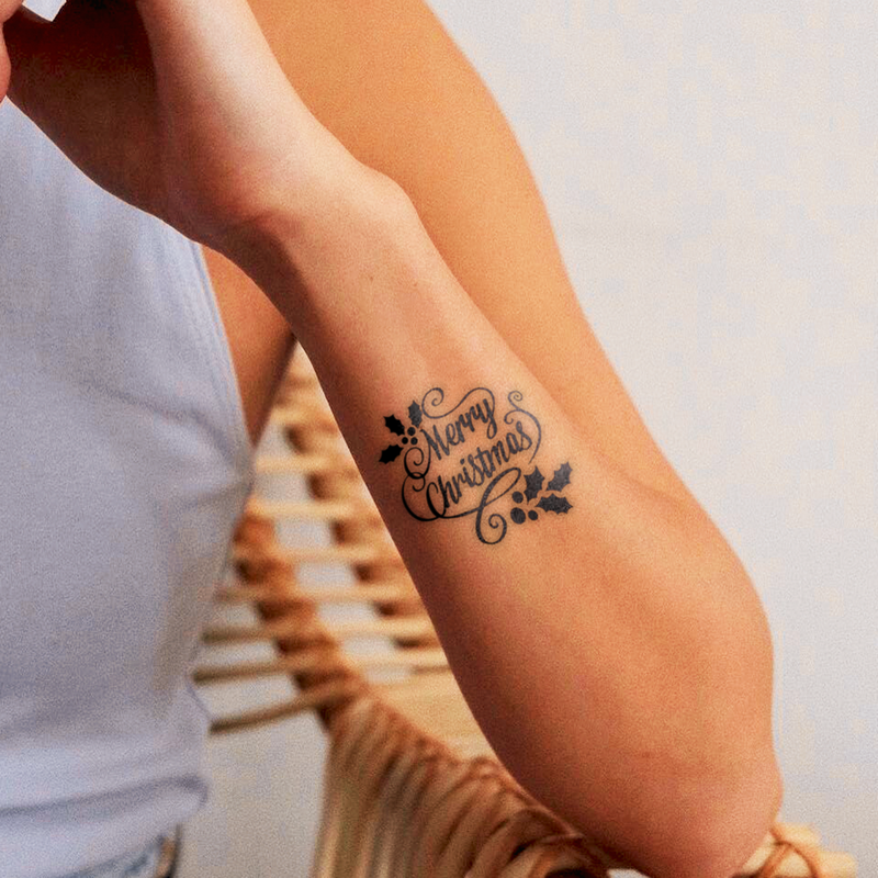 Tattoo of 'Merry Christmas' on a person's arm with a blurred background