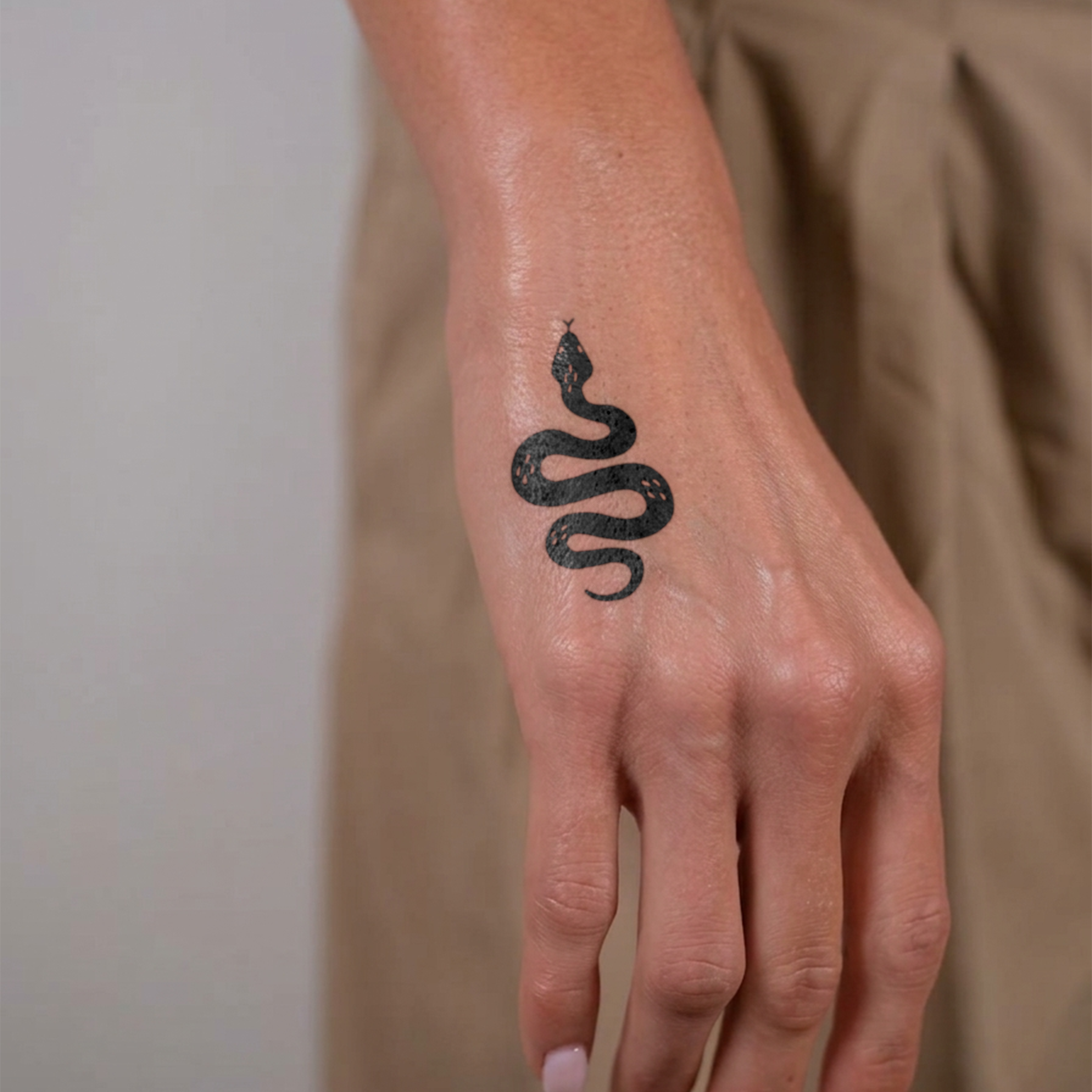 Hand with a black snake tattoo on a plain background