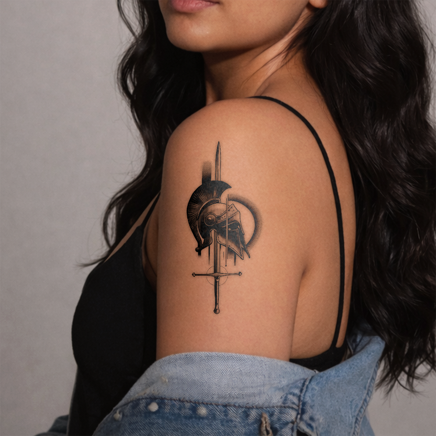 Woman with a tattoo of a helmet and sword on her shoulder against a gray background