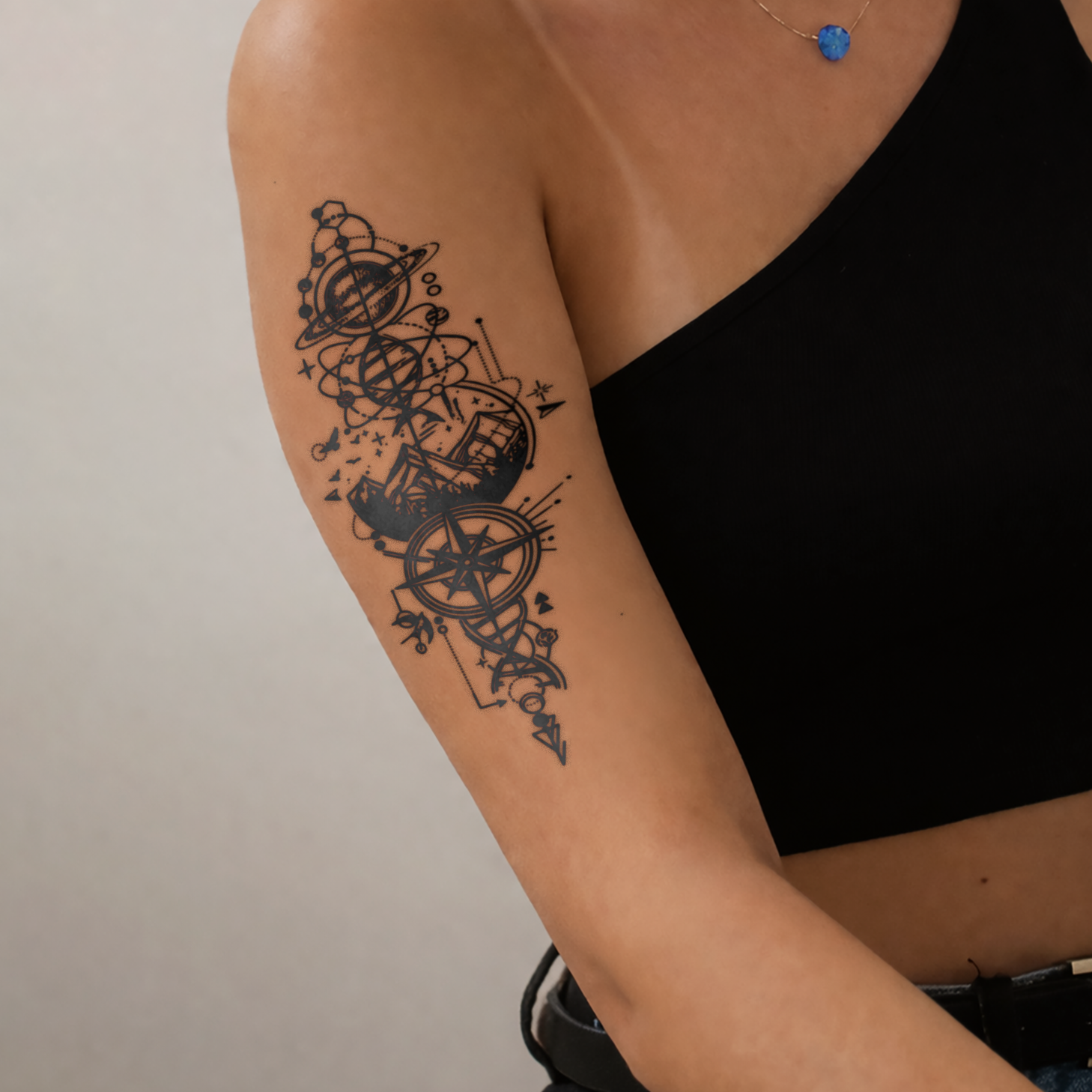 Person wearing a black sleeveless top with a detailed arm tattoo on a neutral background