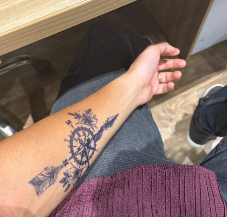 Person with a tattoo on their arm sitting on a wooden bench.