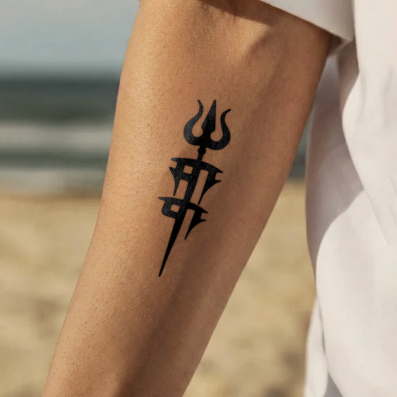Black trident tattoo on a person's arm with a blurred beach background