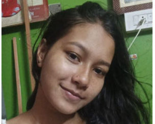 Woman with long hair wearing a white top in front of a green wall with posters.
