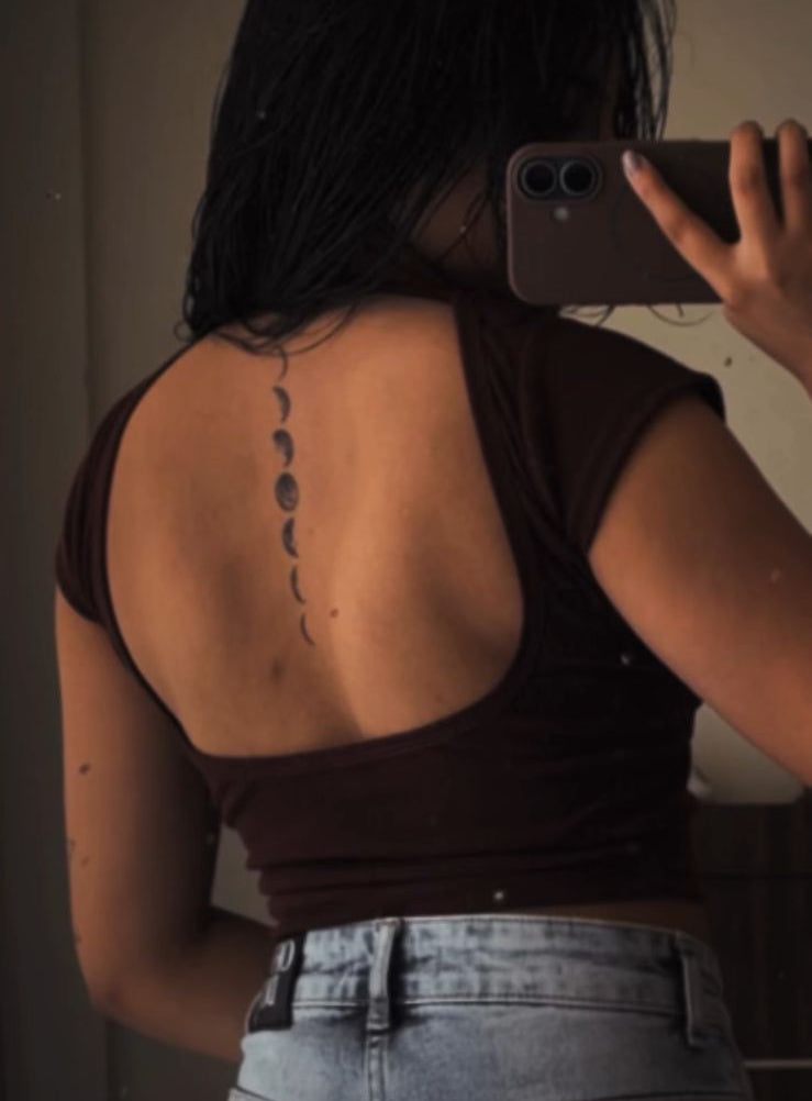Person taking a mirror selfie showing a back tattoo of moon phases.
