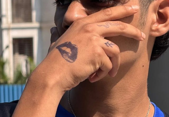 Person with styled hair and tattoo, with a building in the background