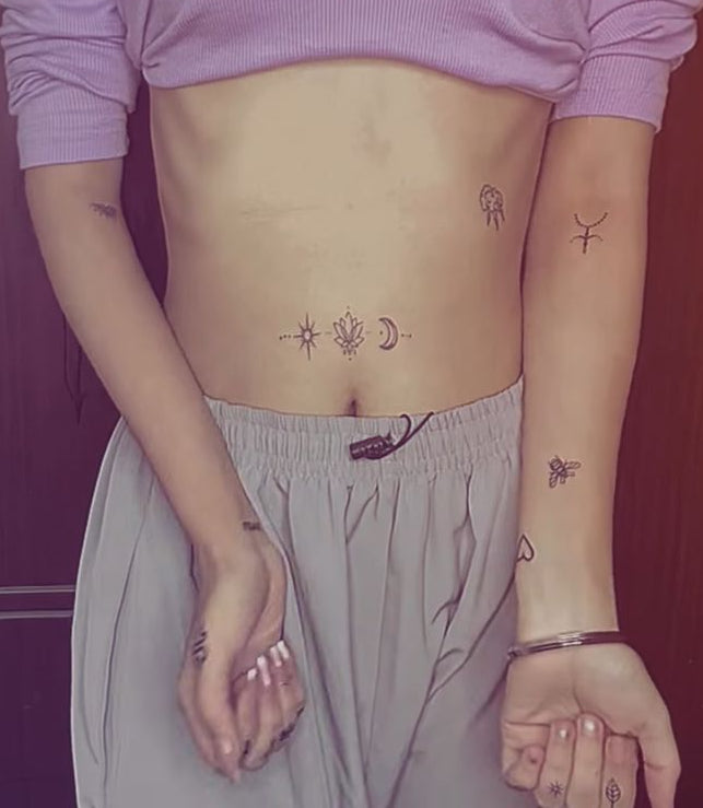 Person with various tattoos on arms and waist against a dark background