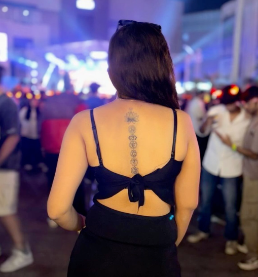 Woman with a back tattoo at a nighttime event with blurred crowd in the background