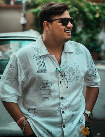 Man wearing sunglasses and a patterned shirt standing outdoors with blurred background